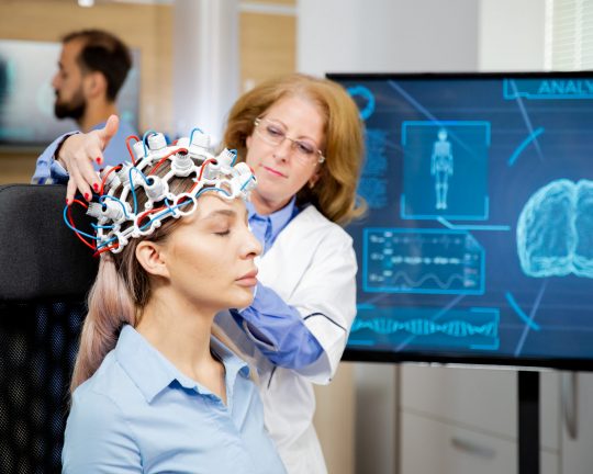 Doctor arranging neurology scanning headset for tests on a female patient