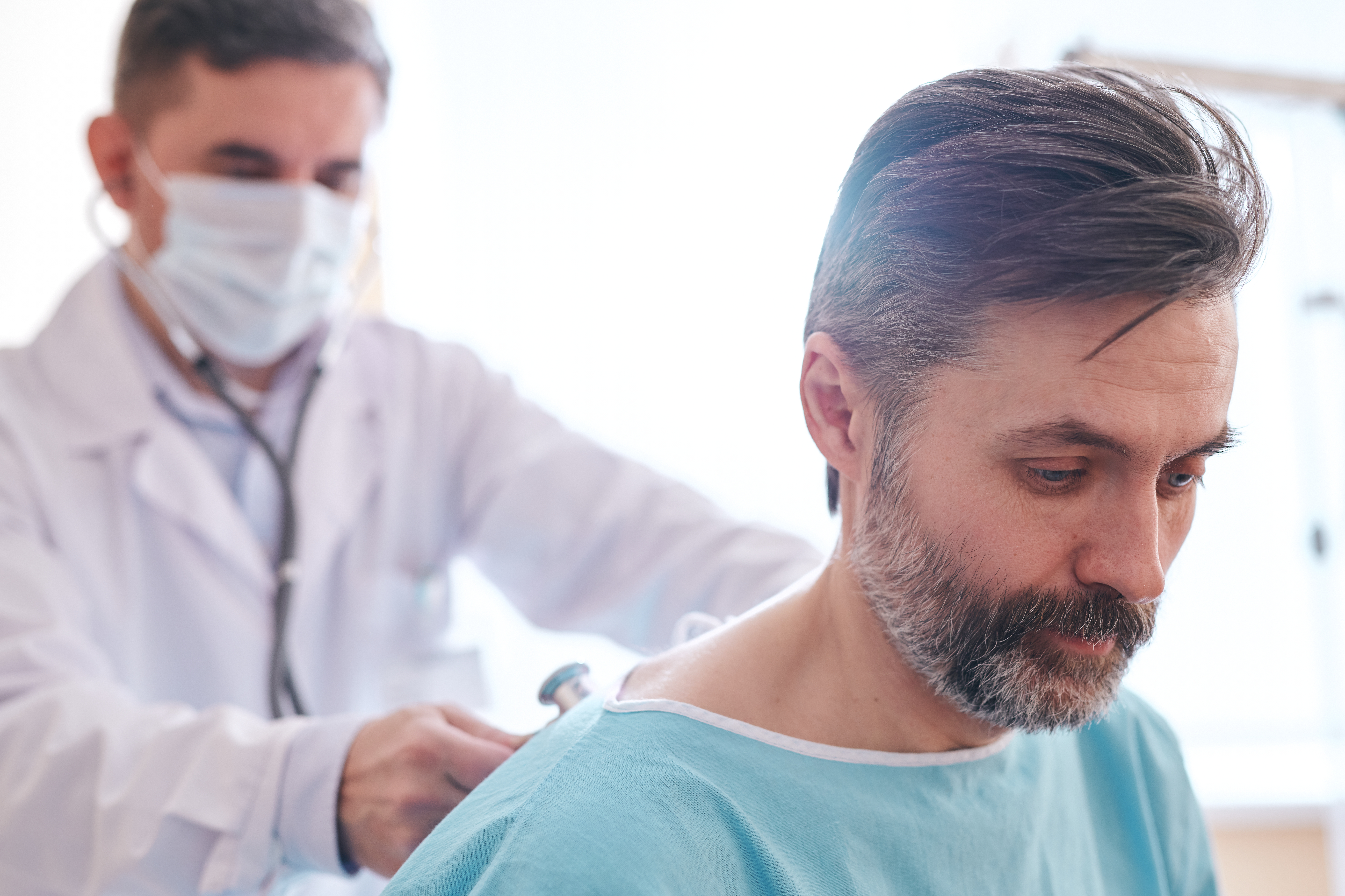 Doctor in surgical mask using stethoscope while listening to patients lungs with stethoscope